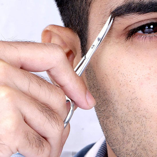 un homme se taillant précieusement les sourcils avec le ciseaux précision