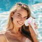 une femme souriante tenant l'épilateur à lumière dans une main au bord d'une piscine 